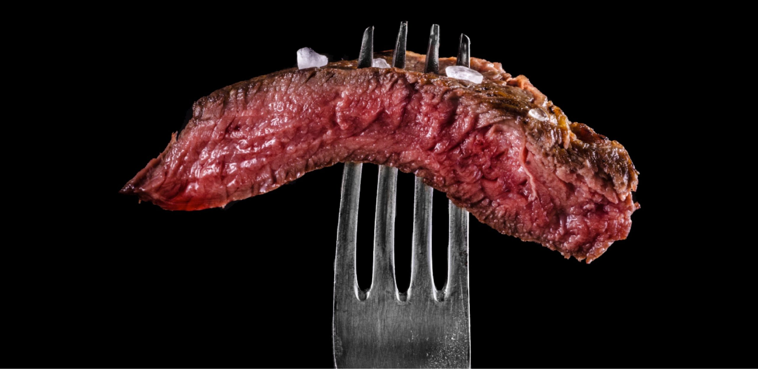 piece of meat skewered with a fork on a black background