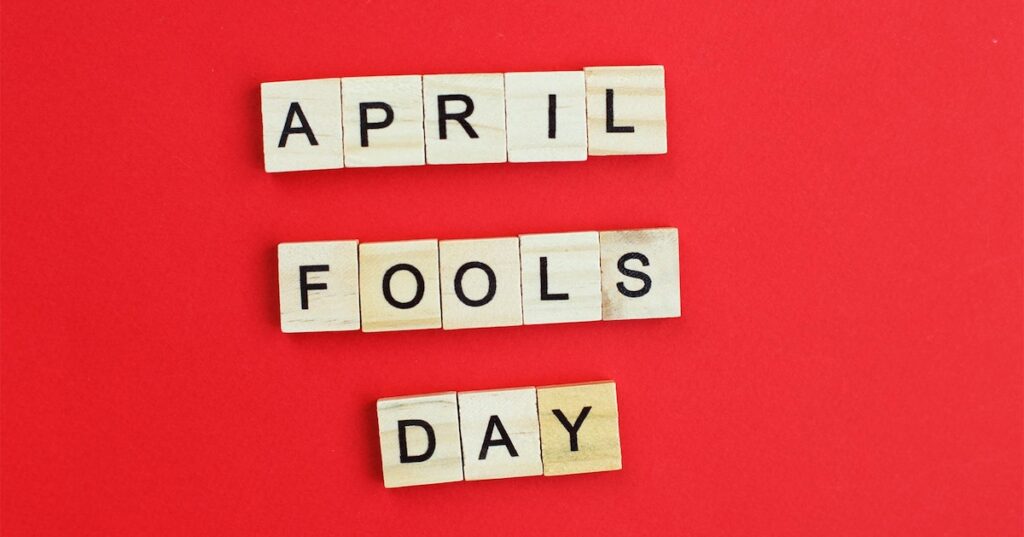 Wooden letter tiles spelling "April Fools Day" on a red background.