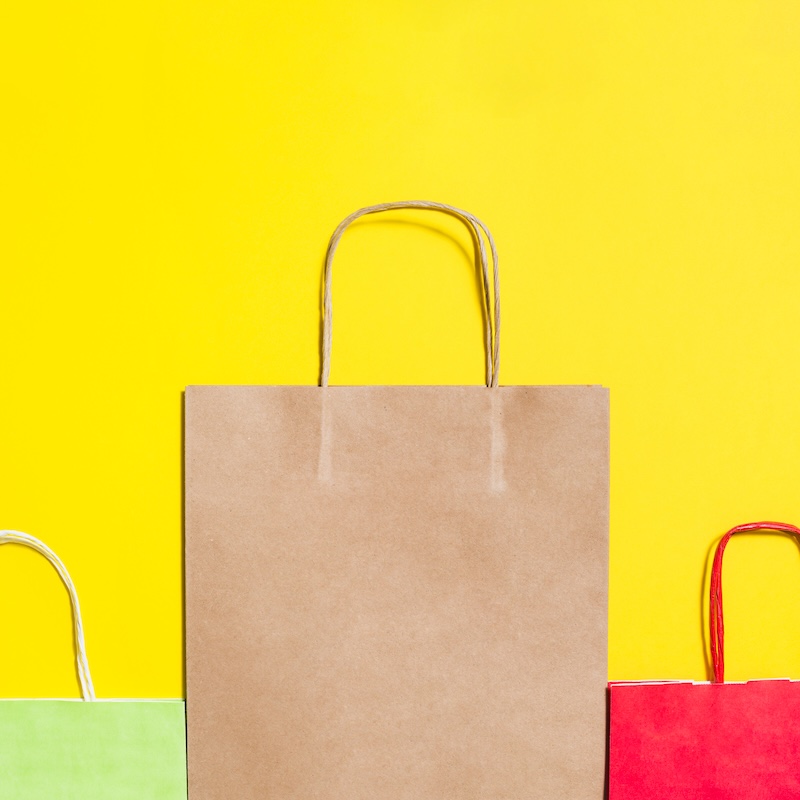 Three shopping bags in brown, green, and red against a yellow background